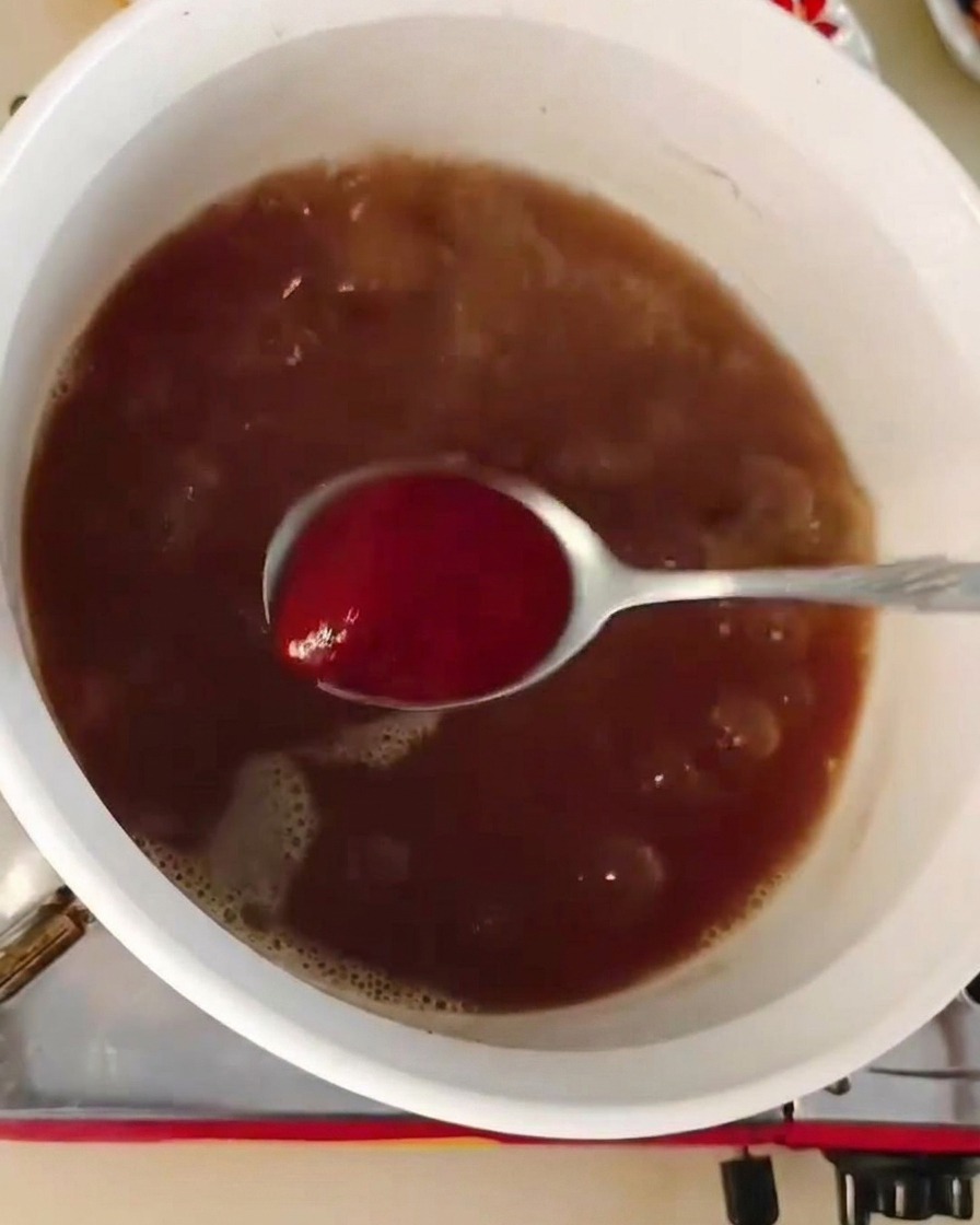 Ein Löffel rote Chilipaste wird in eine brodelnde, dunkelbraune Suppenbasis gerührt.