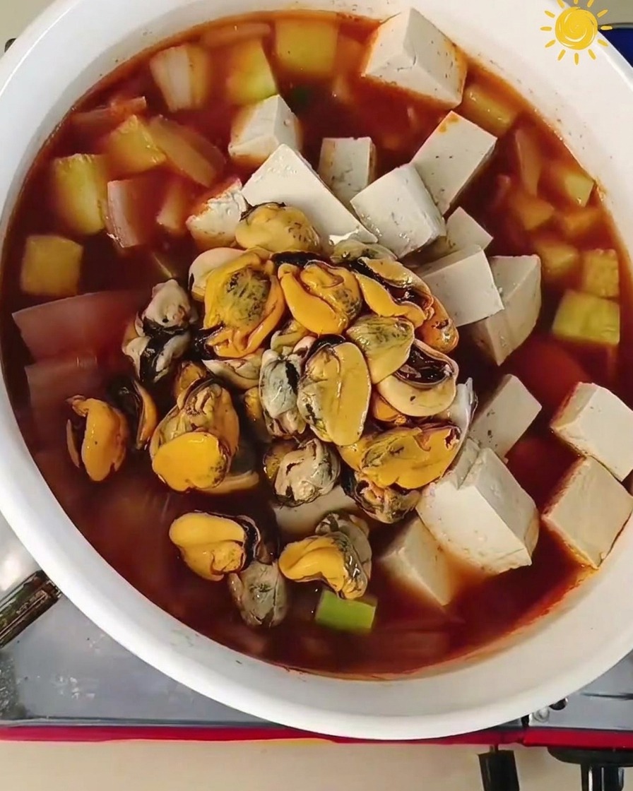 Muschelfleisch und große rohe Garnelen werden in die Mitte eines kochenden Topfes mit Tofu und Gemüse gegeben.