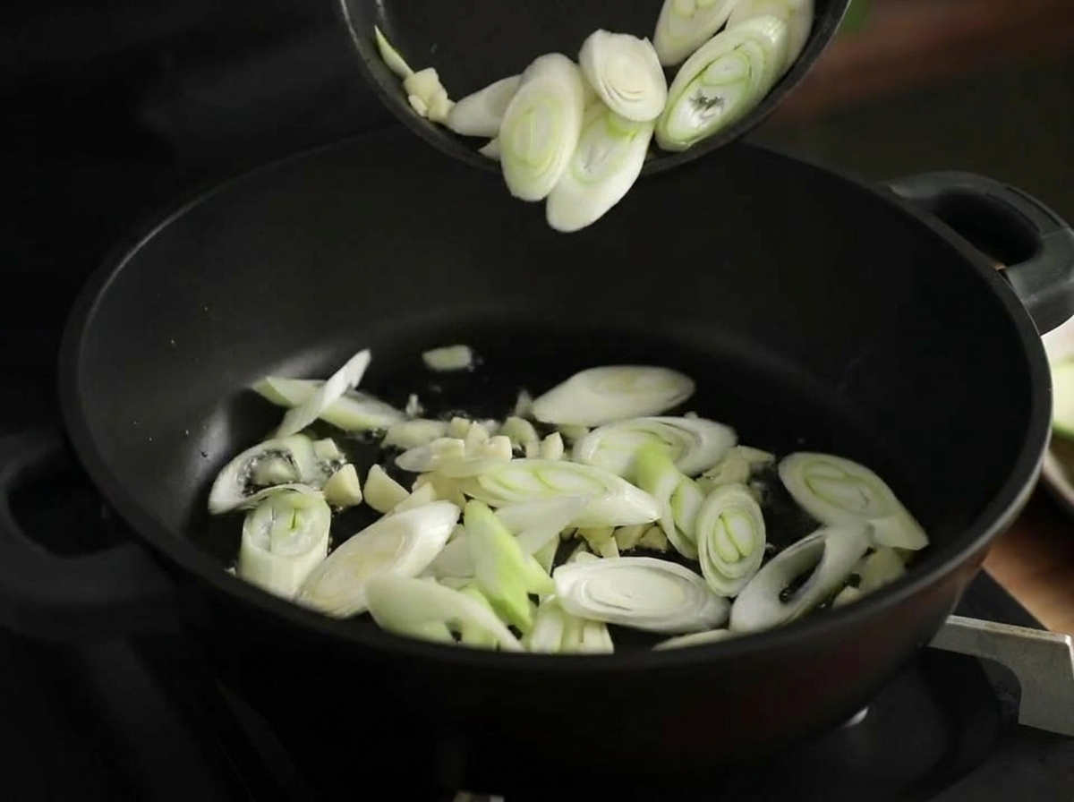 Gehackter Knoblauch und Lauchringe werden in einem schwarzen Topf mit Öl angebraten.