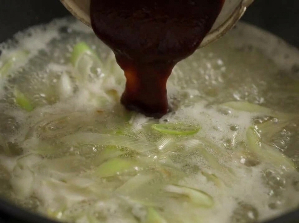 Ein großer Löffel rote Chilipaste wird in die kochende Brühe eingerührt.