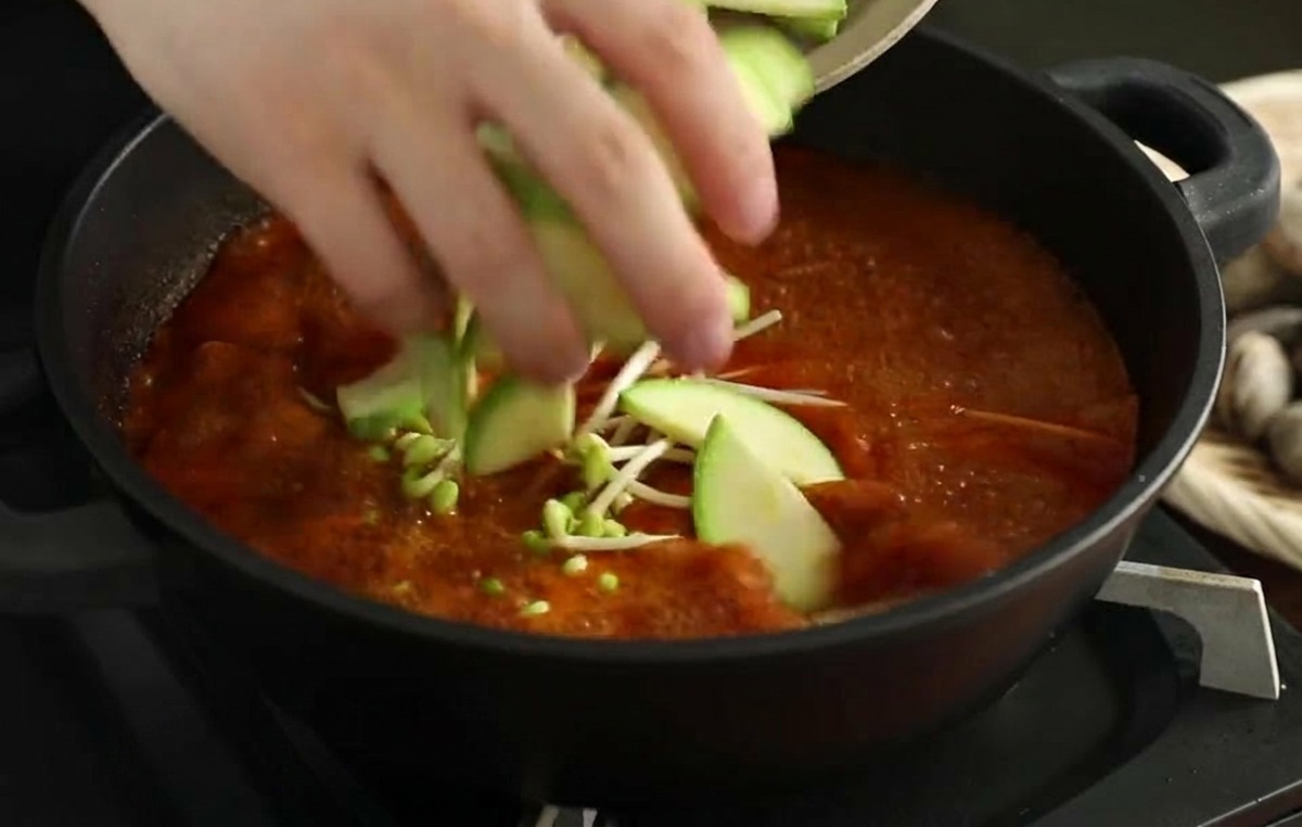 Frische Zucchinischeiben werden in die brodelnde rote Brühe gegeben.
