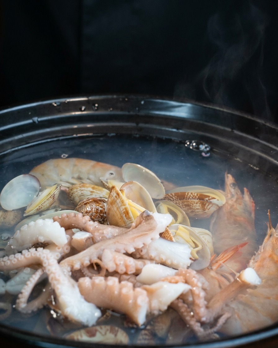 Weiße Tofuscheiben werden vorsichtig auf den Oktopus und die Muscheln im Topf geschichtet.