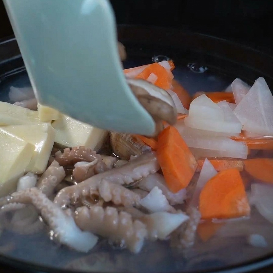 Frische Shiitake-Pilze werden zu der sprudelnden Suppe mit Tofu, Rettich und Karotten hinzugefügt.