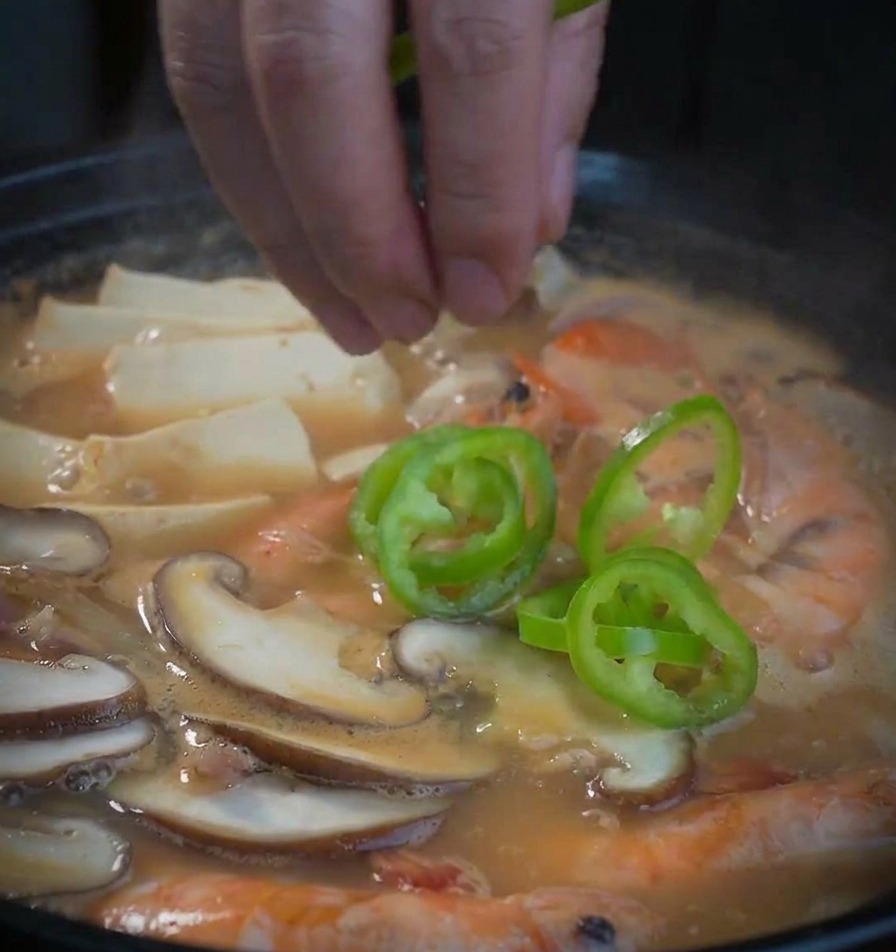 Grüne Paprikaringe werden von Hand in den Topf mit der Sojabohnenpasten-Suppe gegeben.
