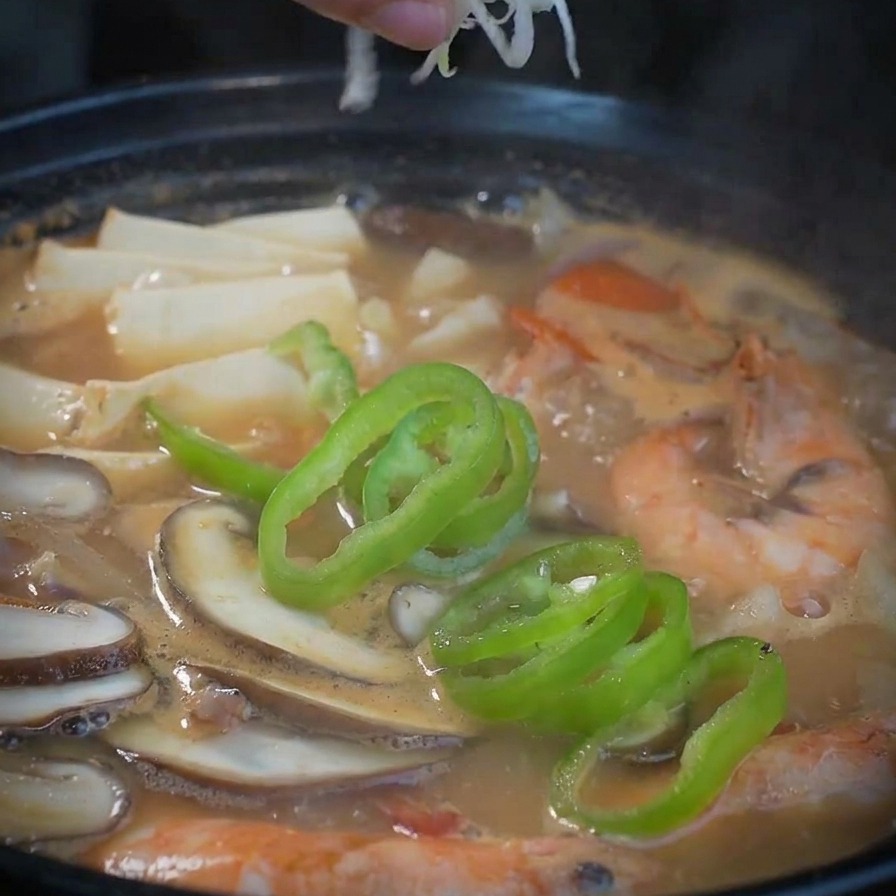 Eine Hand streut geschnittene weiße und grüne Frühlingszwiebeln über die fertige Meeresfrüchtesuppe.