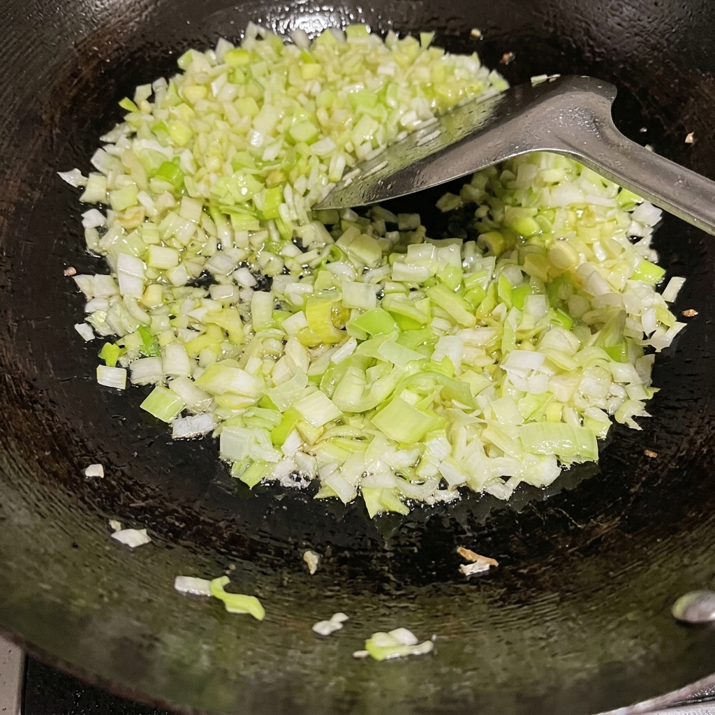 Fein gehackte Frühlingszwiebeln werden in einem schwarzen Wok mit einem Metallspatel angebraten.