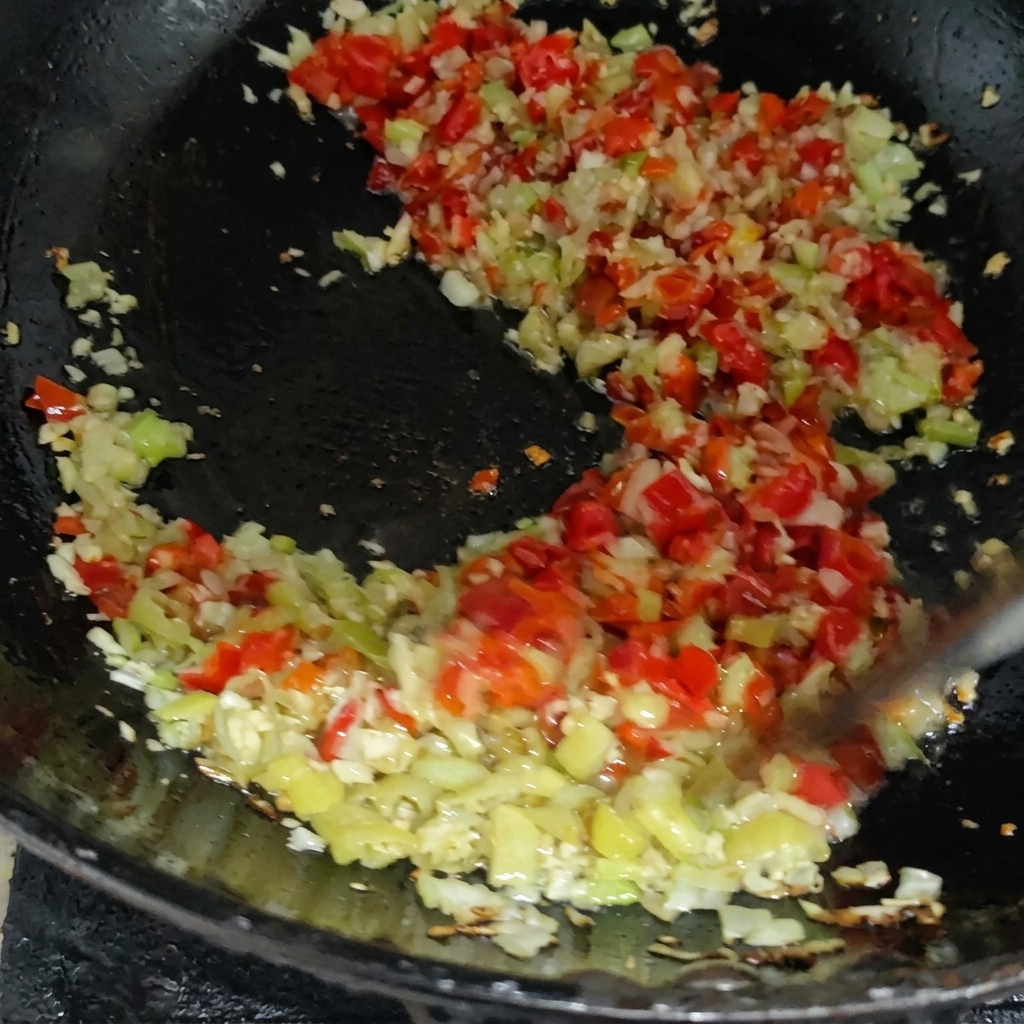 Eine bunte Mischung aus gehackten roten und grünen Chilis wird mit anderen Aromen in einer Pfanne angebraten.