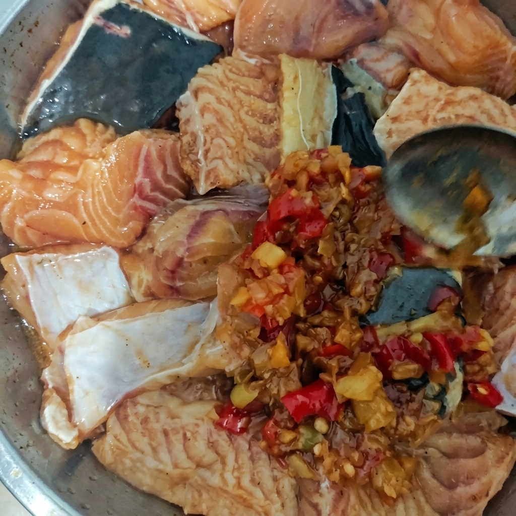 Ein Metallteller mit rohen Fischstücken wird mit einer dicken, stückigen Chili-Knoblauch-Sauce bestrichen.