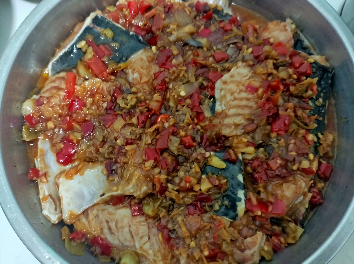 Ein Dämpfeinsatz aus Edelstahl mit Fischstücken, die mit einer leuchtend roten Chilisauce bedeckt sind.