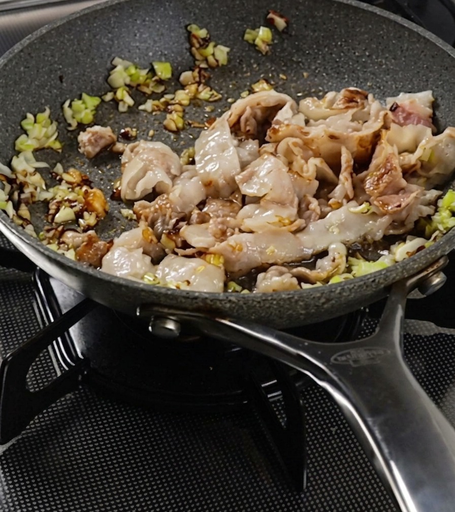Schweinebauch und Zwiebeln werden in einer Pfanne gerührt, bis das Fleisch eine braune Kruste bekommt.