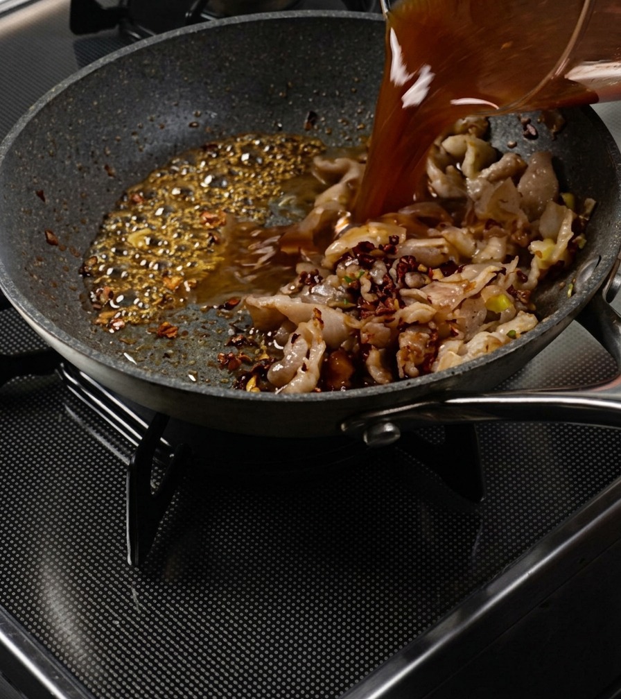 Braune Sauce wird aus einem Becher in die Pfanne zu Fleisch und blubberndem Karamell gegossen.