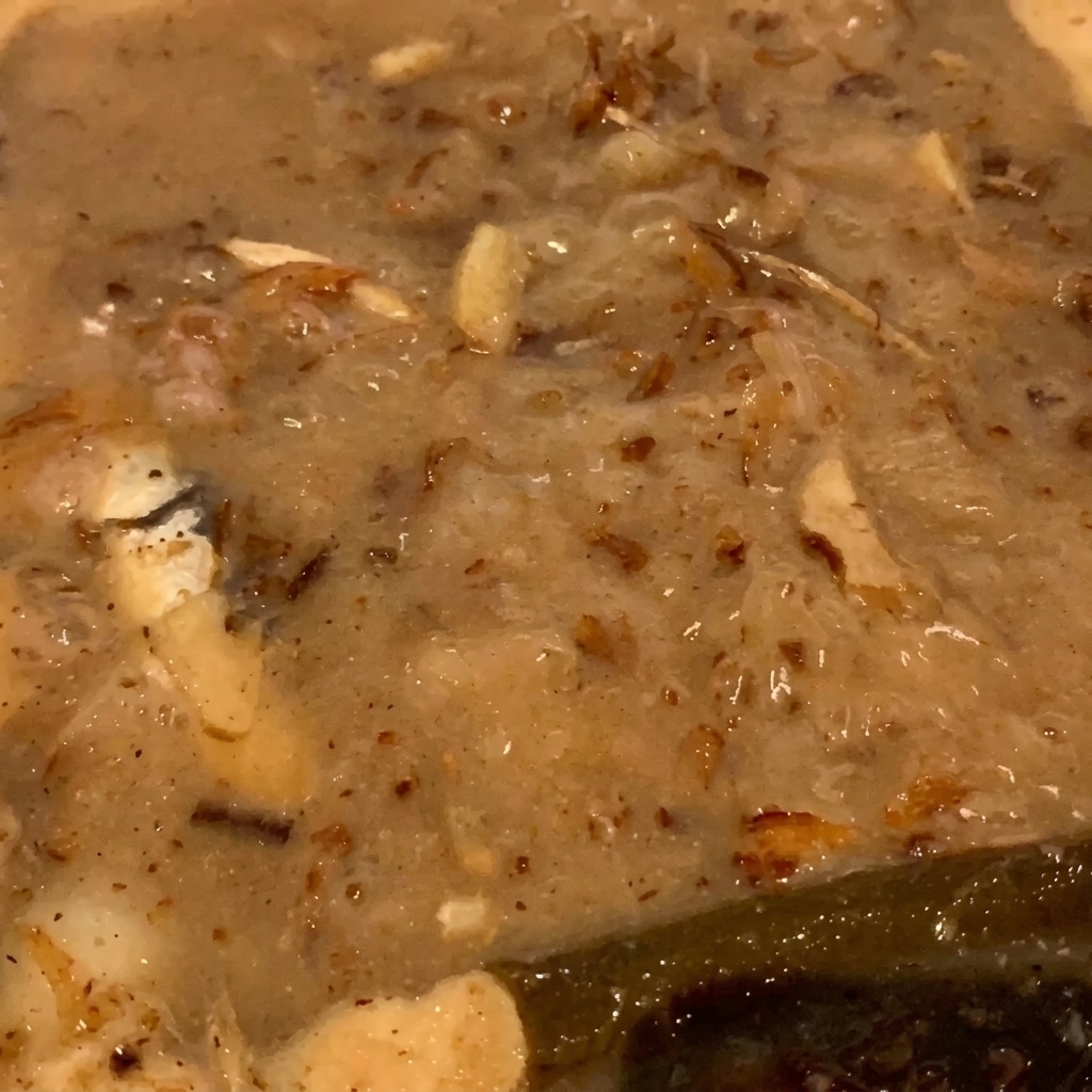 Nahaufnahme von Fischflocken und kleinen Fischen, die in einer sämigen, hellbraunen Flüssigkeit leicht blubbern.