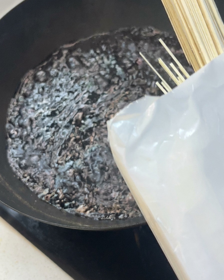 Ein Bündel trockene weiße Nudeln wird in einen Wok mit kochendem Wasser gegeben.