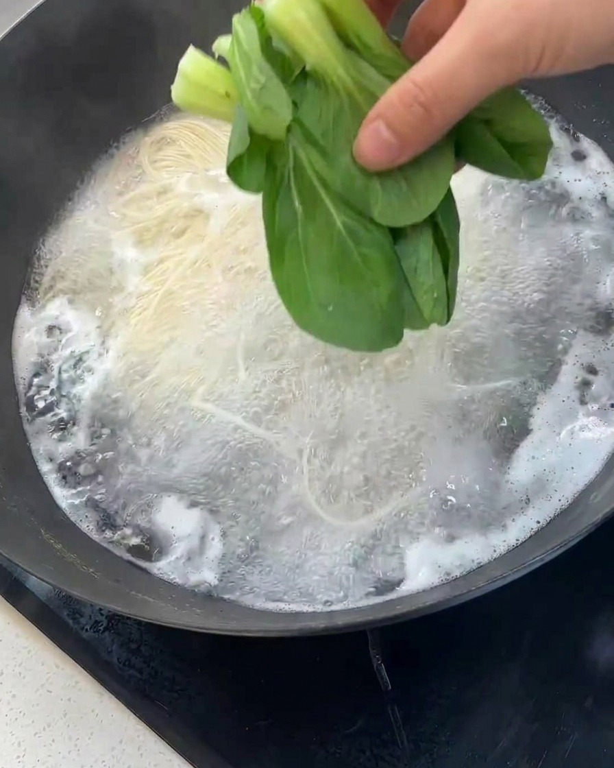 Frischer grüner Bok Choy wird zu den kochenden Nudeln in den Wok gegeben.