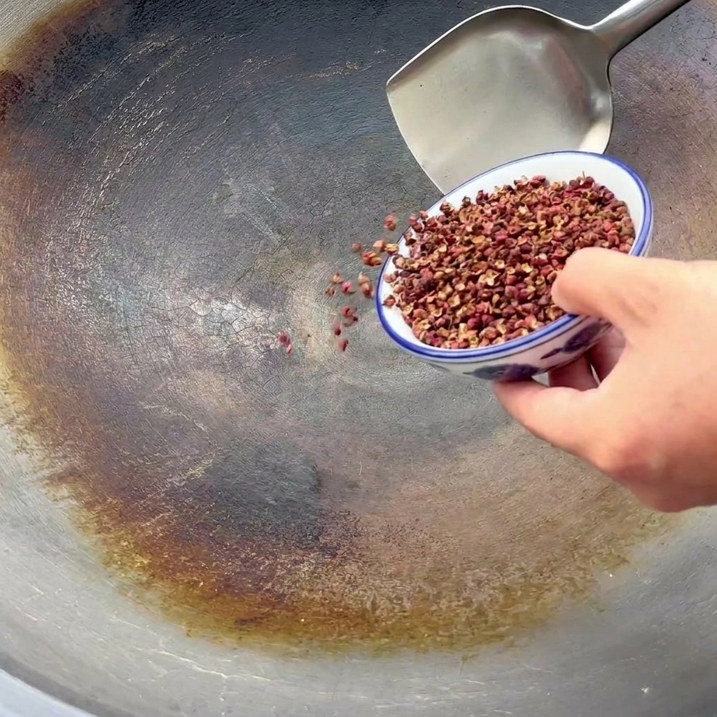 Sichuan-Pfefferkörner werden aus einer kleinen blau-weißen Schale in einen großen Wok zum Rösten geschüttet.