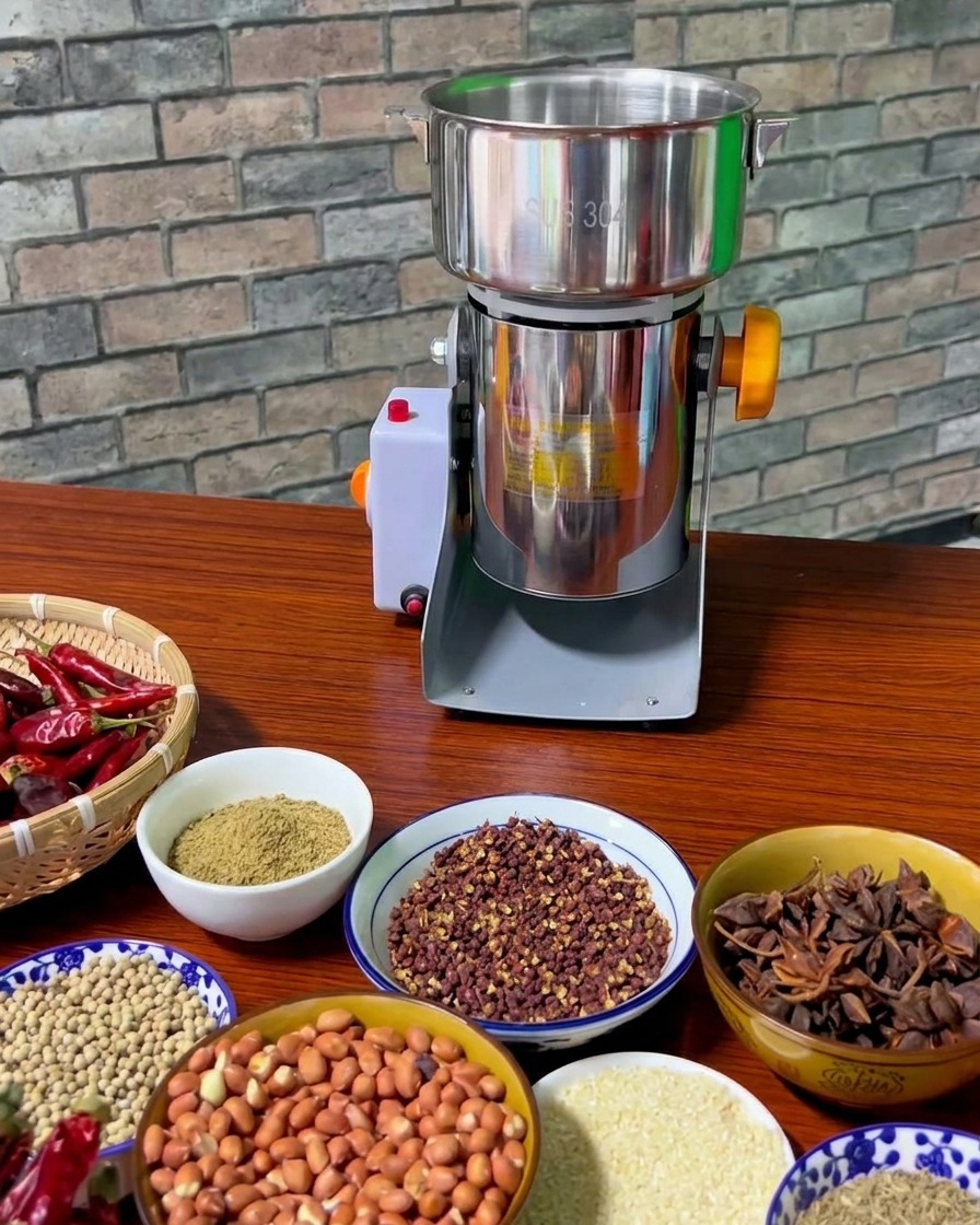 Verschiedene Schalen mit geröstetem Sichuan-Pfeffer, Erdnüssen, Sternanis und Fenchelsamen auf einem Holztisch neben einer elektrischen Gewürzmühle.