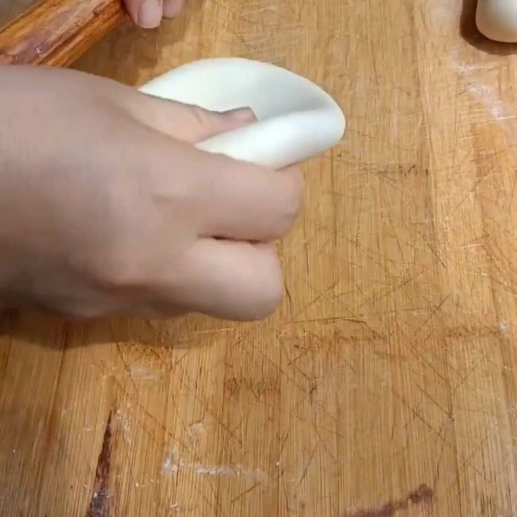 Eine Hand flacht ein Teigstück mit einem Nudelholz zu einer dicken Scheibe auf einem Holzbrett ab.