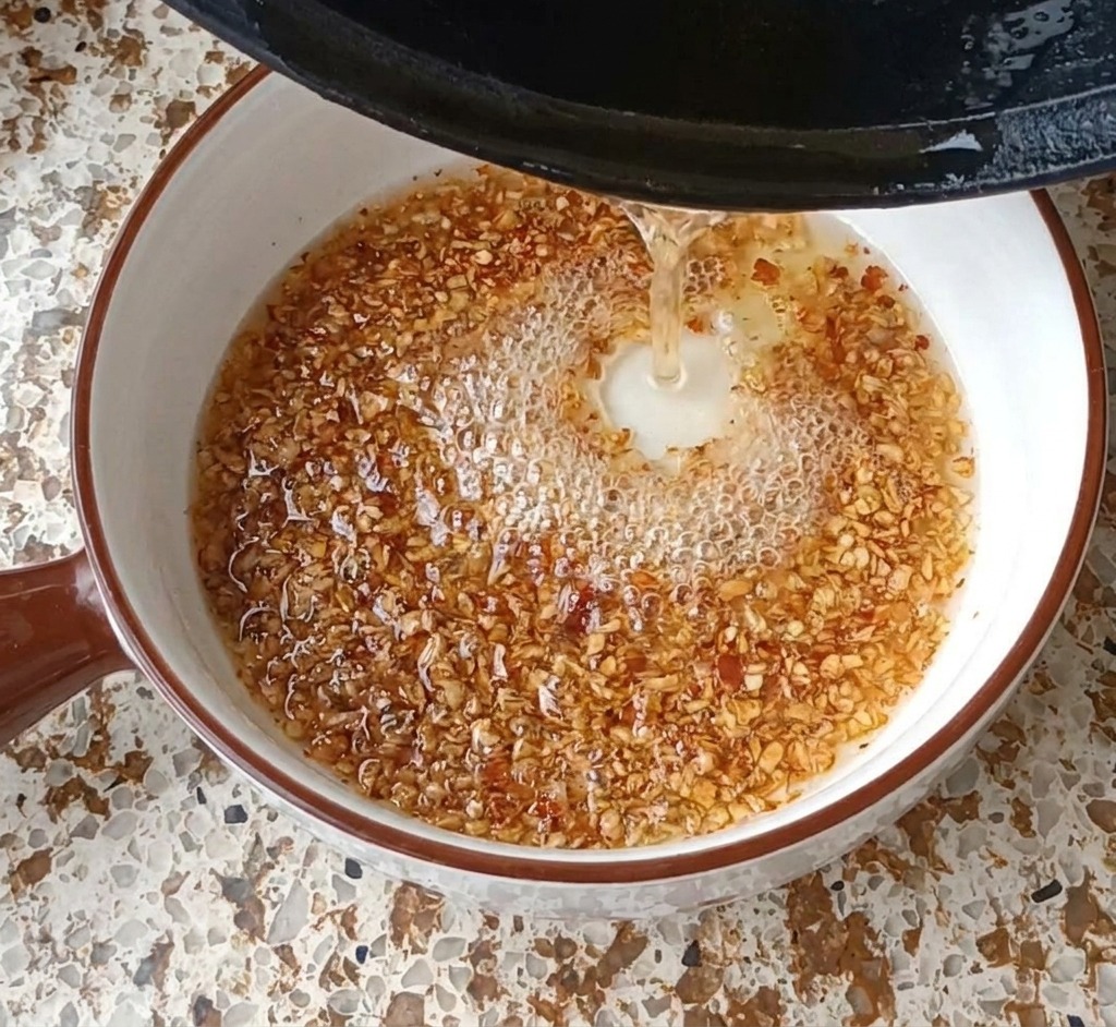 Heißes Öl wird über Knoblauch und Chiliflocken gegossen, wodurch Blasen und Schaum entstehen.