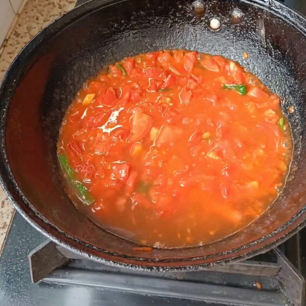 Tomaten und Frühlingszwiebeln köcheln in Wasser in einem schwarzen Wok auf einem Gasherd.