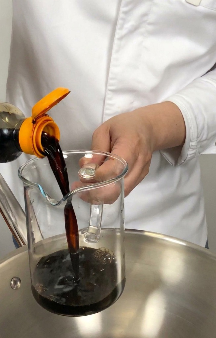 Dunkle japanische Sojasauce wird aus einer Flasche in einen Messbecher über einem Edelstahltopf gegossen.