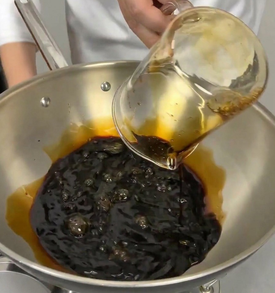 Ein Messbecher gießt klaren japanischen Kochwein in einen Topf mit dunkler Sojasauce.