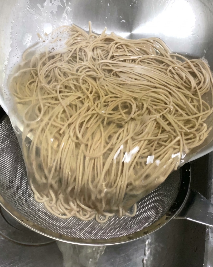 Gekochte Buchweizennudeln werden aus einer Schüssel in ein Sieb im Spülbecken gegossen, um das Wasser abtropfen zu lassen.