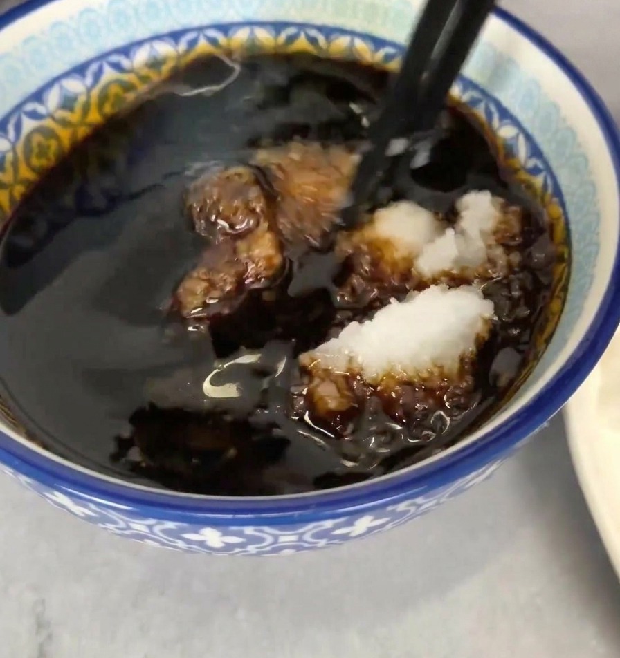 Eine blau-weiße Schüssel mit dunkler Dip-Sauce, in die geriebener Rettich mit schwarzen Essstäbchen eingerührt wird.