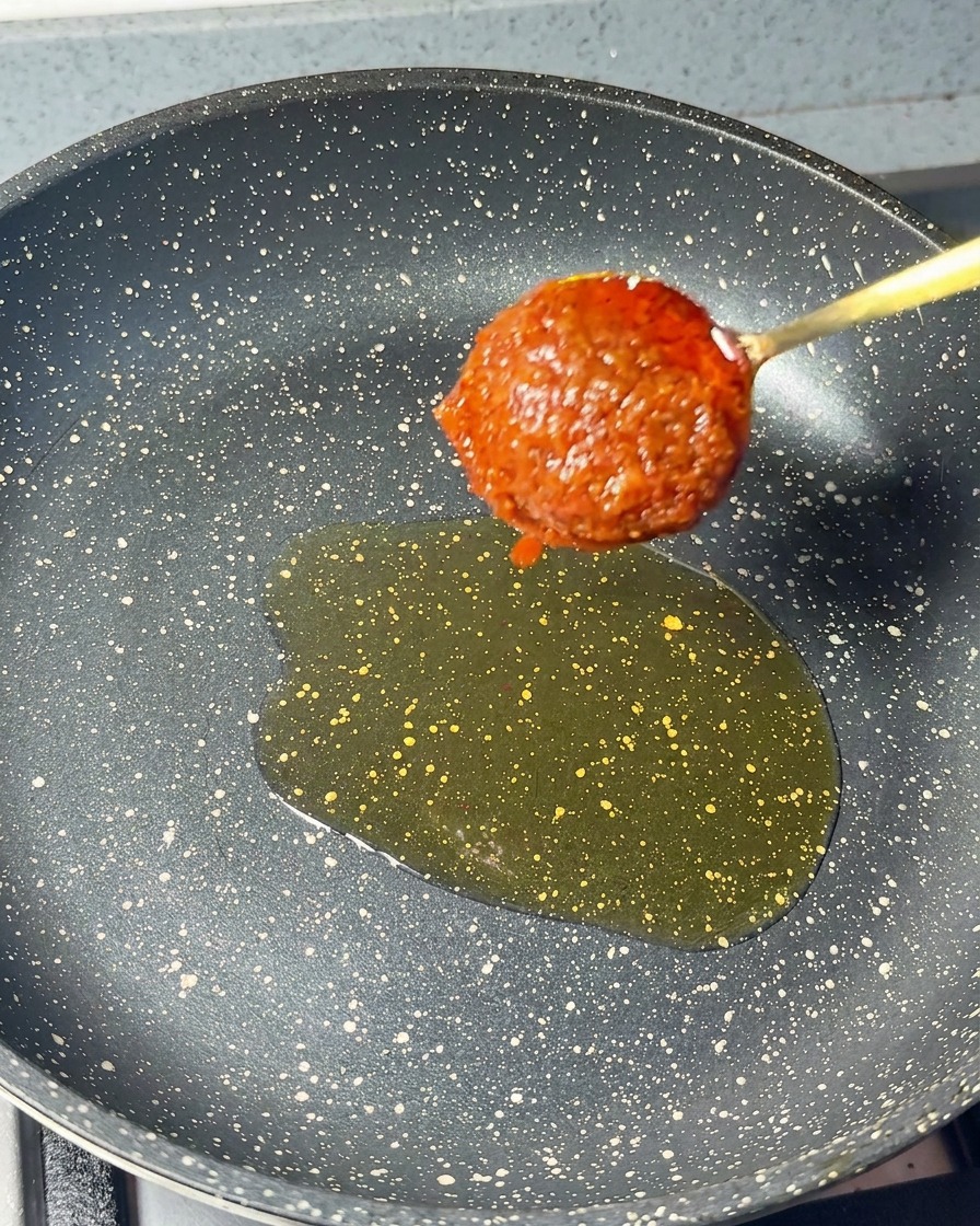 Ein Löffel dicker roter Garnelenpaste wird in eine Pfanne mit Sesamöl gegeben.