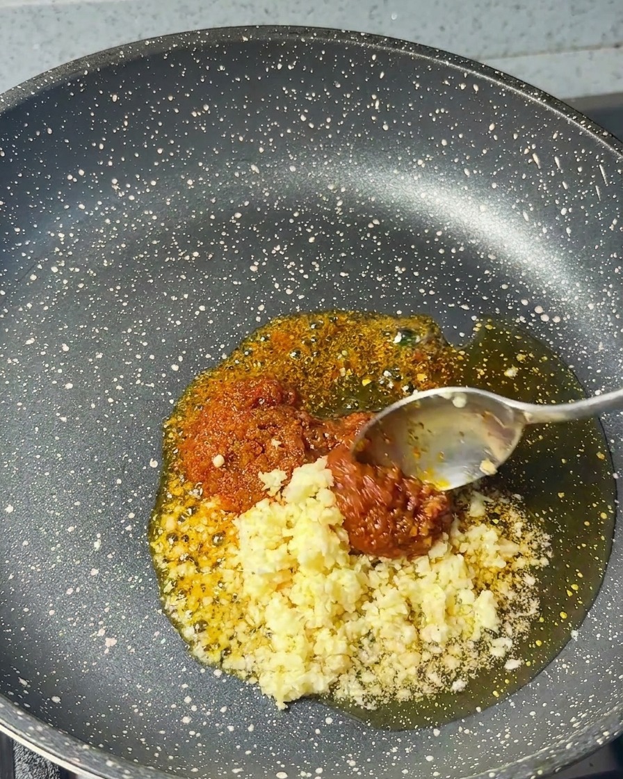 Gehackter Knoblauch wird zu der Garnelenpaste und dem Sesamöl in die Pfanne gegeben.