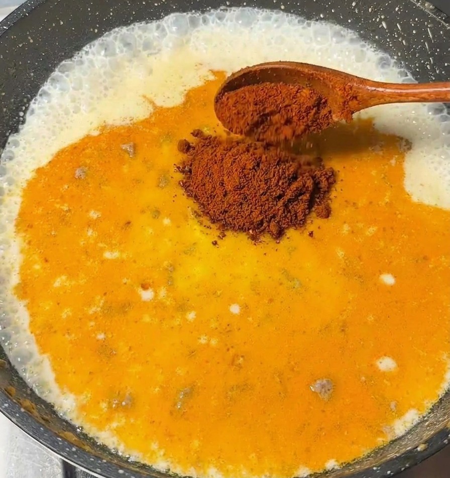 Ein Holzlöffel gibt Curry-Roux-Stücke in die köchelnde Milchbasis.