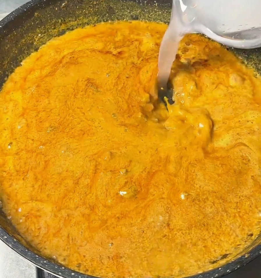 Eine klare Flüssigkeit wird aus einer kleinen Schale in die köchelnde Curry-Dipsauce gegossen.