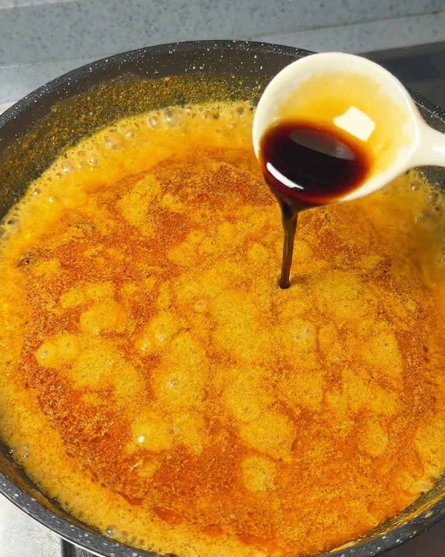 Ein weißer Löffel gießt dunkle Sojasauce in die blubbernde Curry-Dipsauce.