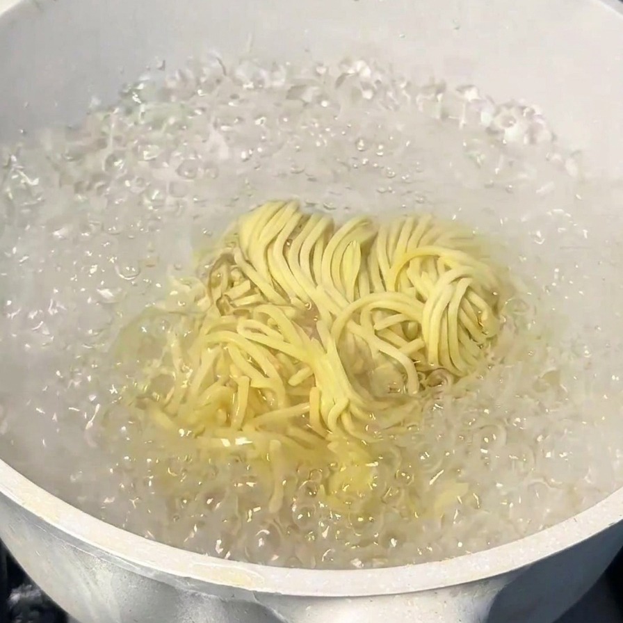 Ein Bündel gelbe japanische Ramen-Nudeln kocht in einem Topf mit sprudelndem Wasser.