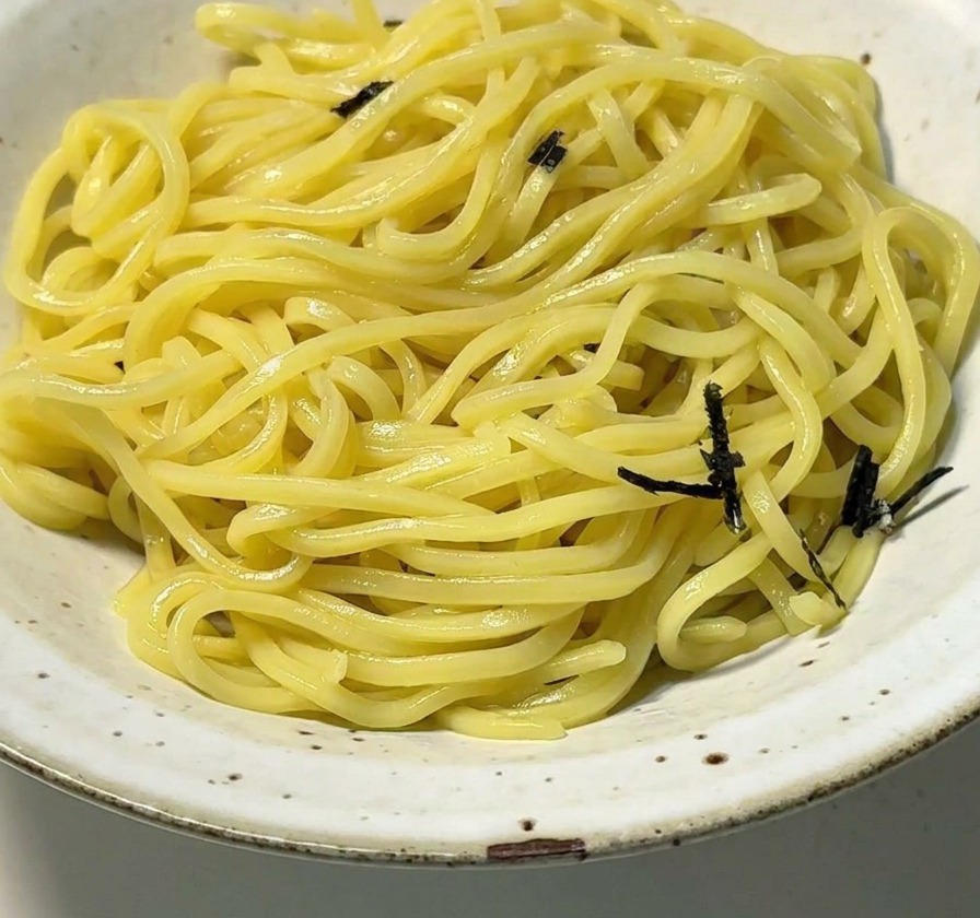 Eine weiße Schale mit Ramen-Nudeln wird mit Streifen aus schwarzem Nori belegt.