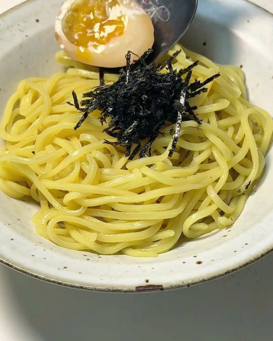 Nahaufnahme einer Schale mit Nudeln und Nori, auf die ein halbiertes Ei mit flüssigem Eigelb gelegt wird.