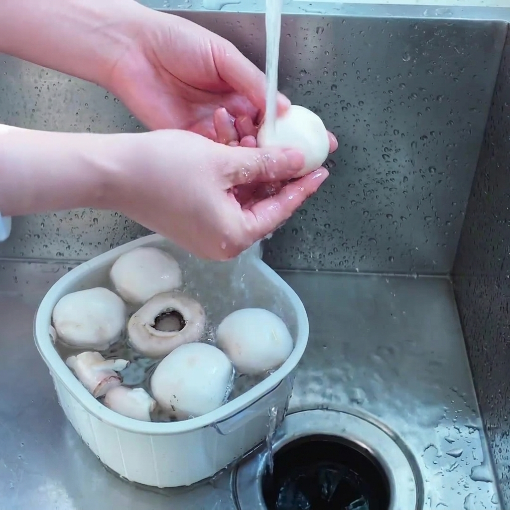 Eine Person wäscht weiße Champignons in einem weißen Sieb unter fließendem Leitungswasser.