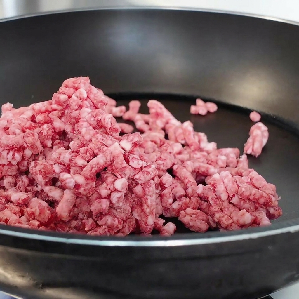 Rohes Rinderhackfleisch wird in einer schwarzen beschichteten Pfanne angebraten und zerkleinert.