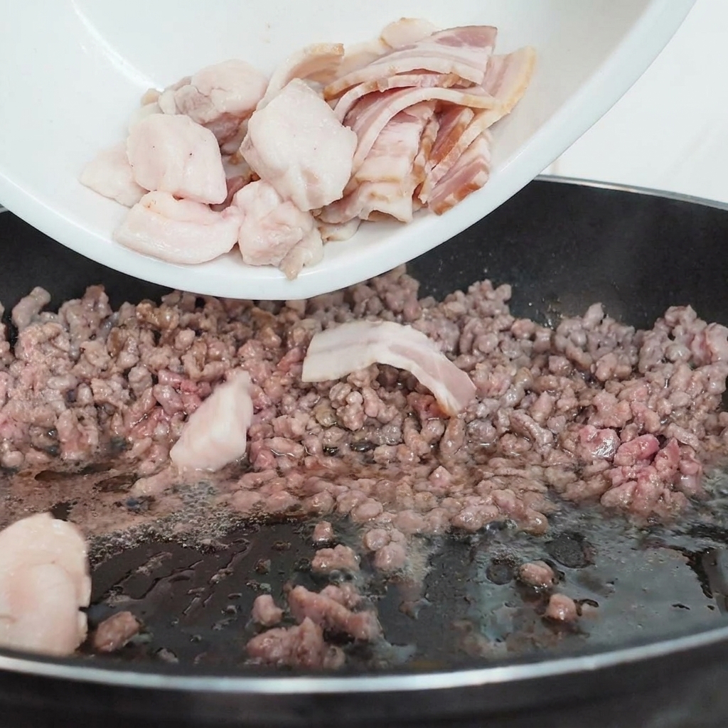 Geschnittene Pilze werden von einem Teller in eine Pfanne mit angebratenem Hackfleisch gegeben.