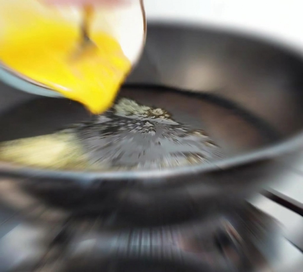 Eiermasse wird aus einer Schüssel in eine heiße Pfanne mit geschmolzener Butter gegossen.