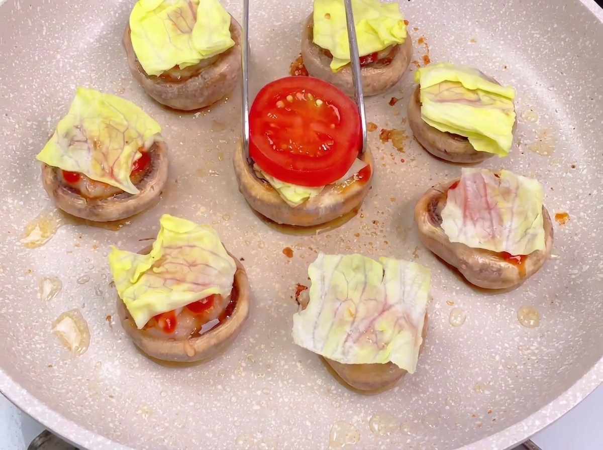 Eine Zange legt eine Tomatenscheibe auf den Burger-Boden mit Salat und Sauce.