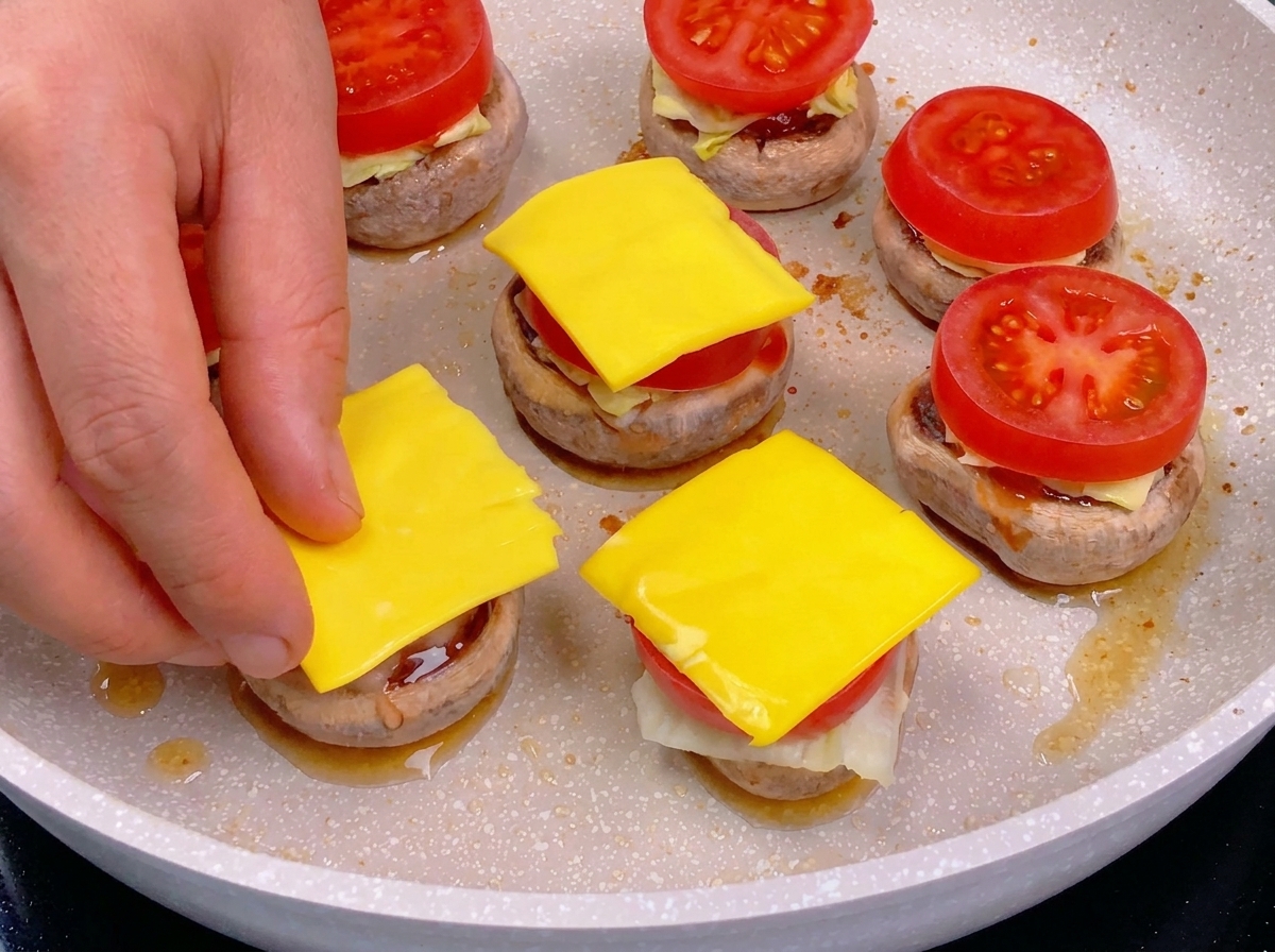 Eine Hand legt ein Quadrat aus gelbem Käse auf eine Tomatenscheibe.