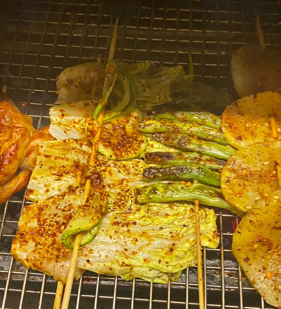 Nahaufnahme von gegrilltem Hähnchen und Gemüse, das mit roter BBQ-Sauce bestrichen und mit Zwiebeln garniert wird.