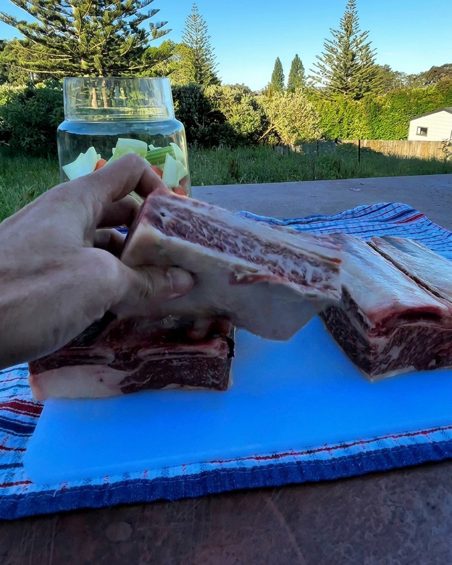 Eine rohe Rinderrippe wird über ein Glasgefäß mit gehacktem Gemüse gehalten.