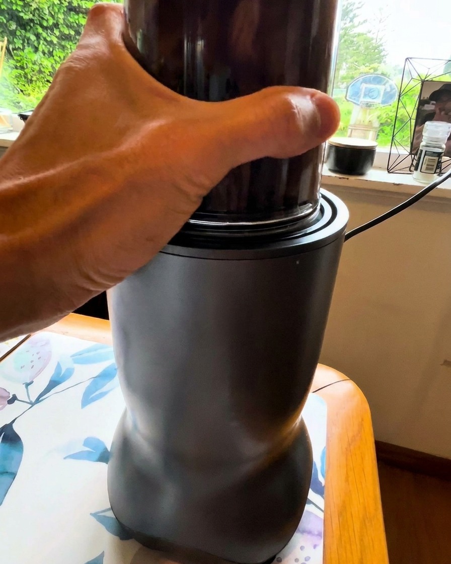 Eine Hand hält den Behälter eines kleinen Mixers, in dem eine dunkle Gemüsemischung püriert wird.