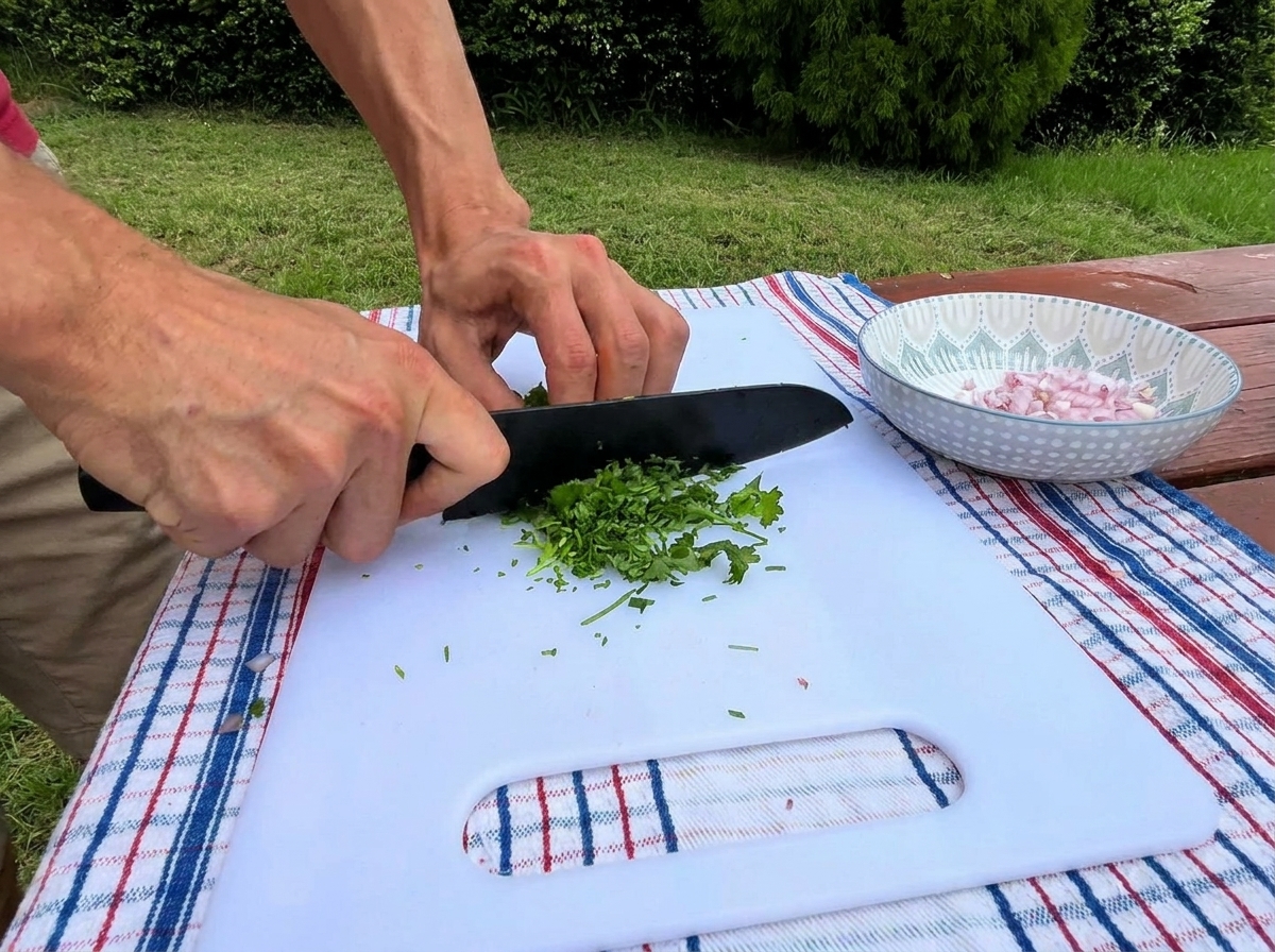 Hände schneiden frische grüne Petersilie mit einem schwarzen Messer auf einem weißen Brettchen, daneben eine kleine Schüssel mit gewürfelten Schalotten.