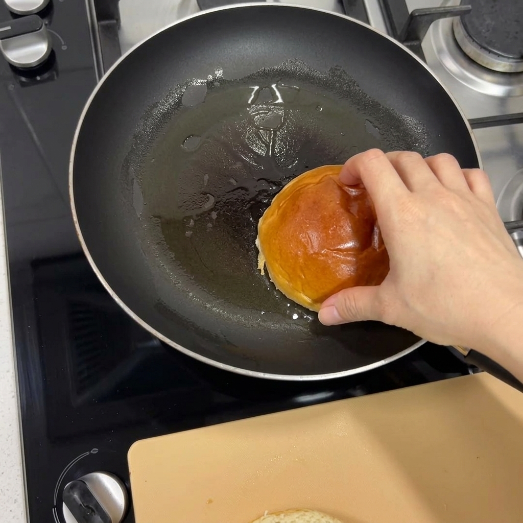 Eine Hand legt ein Brioche-Brötchen in eine erhitzte Pfanne, um es goldbraun anzurosten.