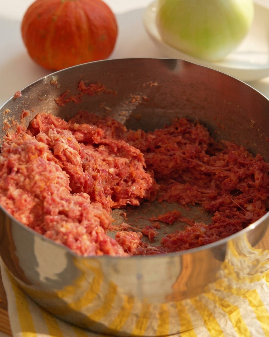 Eine Metallschüssel gefüllt mit einer Mischung aus rohem Rinderhackfleisch, fein gehackten Zwiebeln und Bindemitteln für die Burger-Patties.