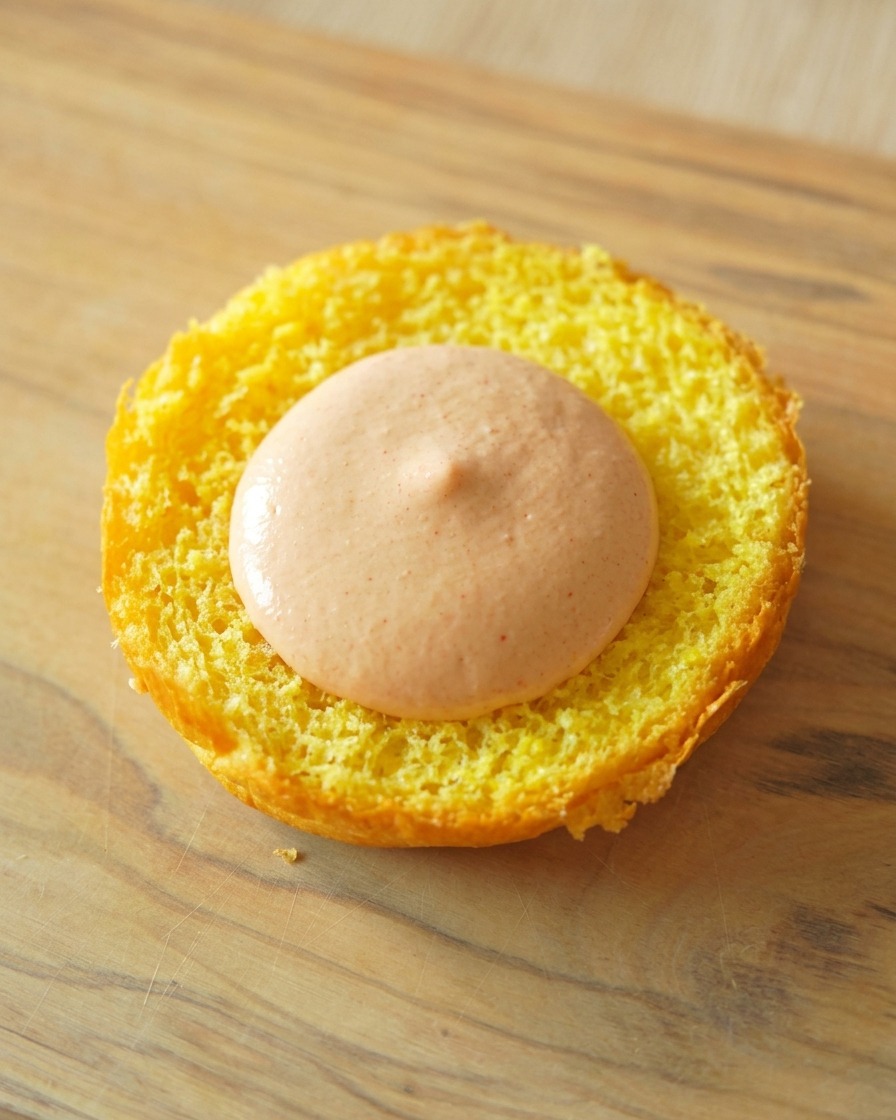 Die getoastete Unterseite eines gelben Brioche-Buns mit einem glatten Klecks orangefarbener Burgersauce in der Mitte.