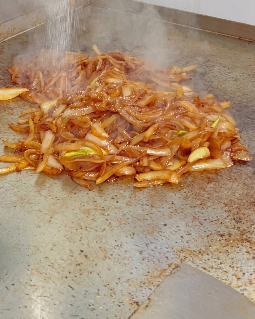 Feines Salz wird über einen Haufen dampfender, glänzender karamellisierter Zwiebeln auf dem Grill gestreut.