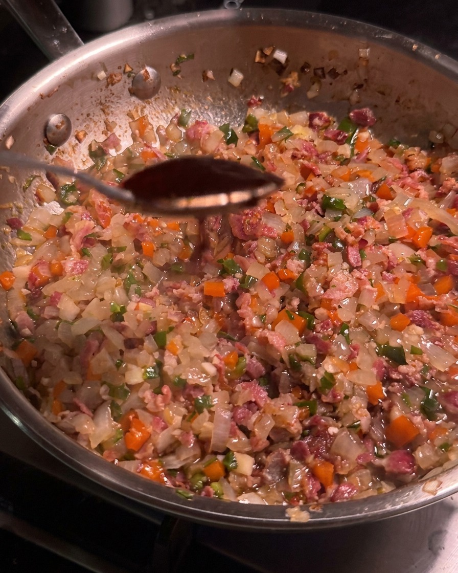 Ein Löffel mit dunkler Chipotle-Sauce über einer Pfanne mit der Bacon-Gemüse-Mischung.